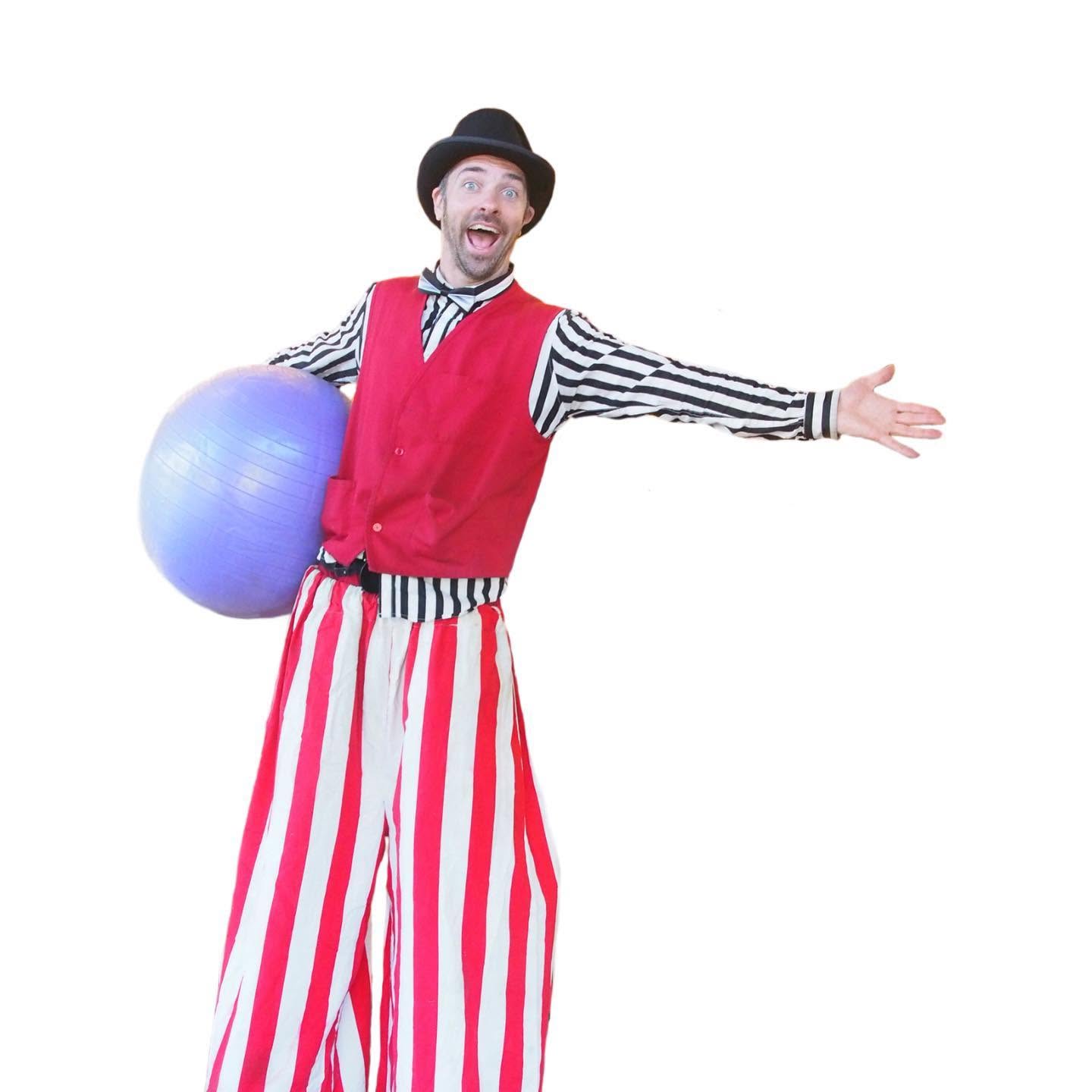 Nick Kane in a striped stilt-walking costume with a purple ball